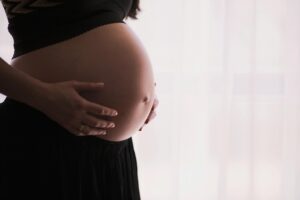 A close-up of a pregnant woman touching her bare belly, expressing warmth and care.